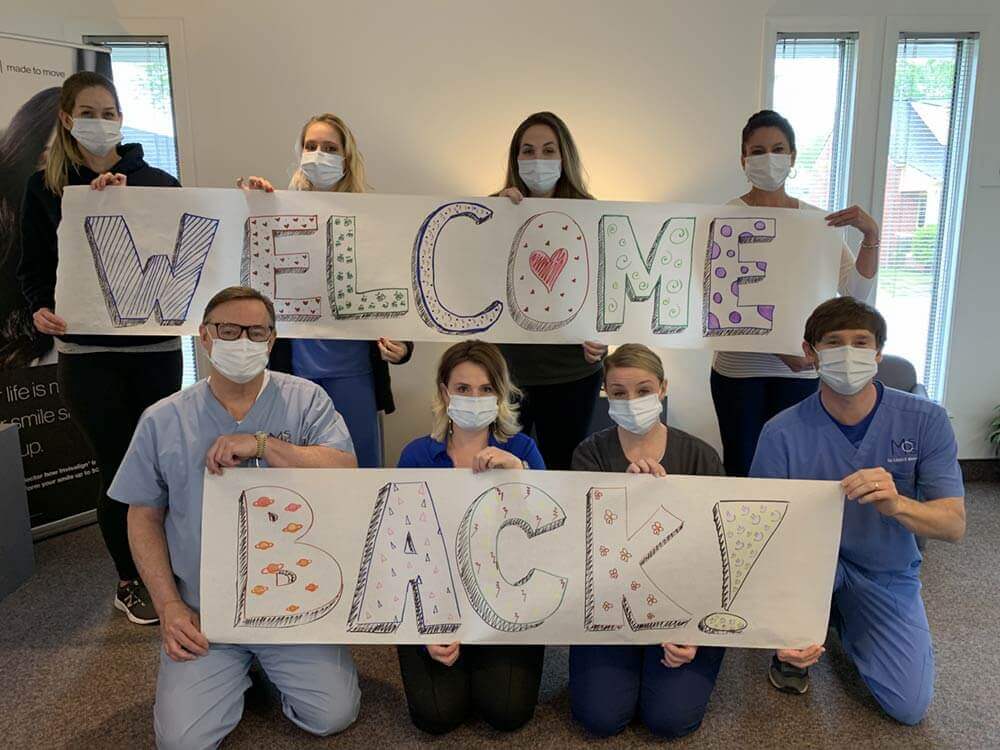 Office Staff with masks holding Welcome Back signs